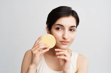 Beyaz tişörtlü güzel kadın ellerinde süngerle makyajı temizliyor.