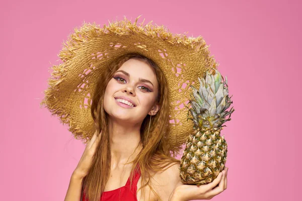 Mulher com uma arma nas mãos de um chapéu de palha maquiagem brilhante frutas exóticas verão fundo rosa — Fotografia de Stock