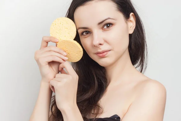 Attraktive Brünette mit nackten Schultern hält Schwämme nahe ihrem Gesicht saubere Haut — Stockfoto