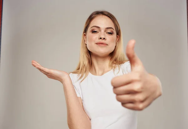 Copy Space szőke nő mutatja a kezét oldalra egy bézs háttér egy fehér póló — Stock Fotó