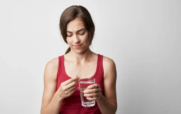 Maquillage femme en rouge t-shirt détient verre d'eau pilule médicaments problèmes de santé — Photo