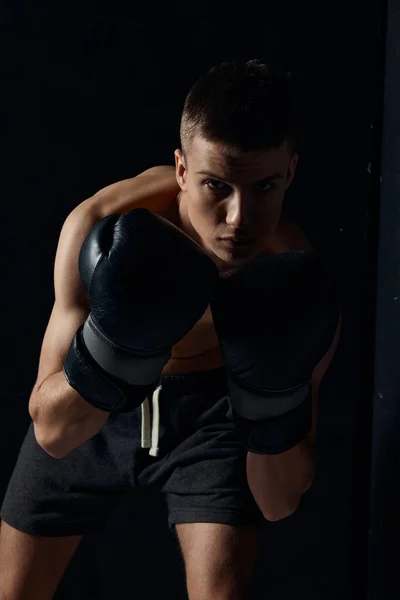 Boxer v černých rukavicích ohnutý na tmavém pozadí kulturista fitness cvičení — Stock fotografie