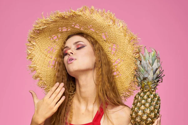 Kvinna med en pistol i händerna på en halm hatt ljus makeup exotiska frukter sommar rosa bakgrund — Stockfoto