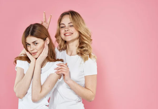 Dos mujeres moda ropa divertido abrazo cuidado rosa fondo — Foto de Stock