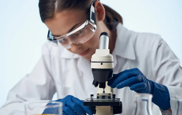Женщина лаборант с микроскопом на столе и очки на лице жидкости во фляжке — стоковое фото
