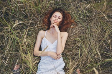 Beyaz elbiseli kızıl saçlı kadın açık hava modelinin samanlığında yatıyor.