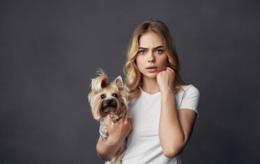 Beyaz tişörtlü neşeli bir kadın elinde küçük bir köpek evcil hayvanı tutuyor.