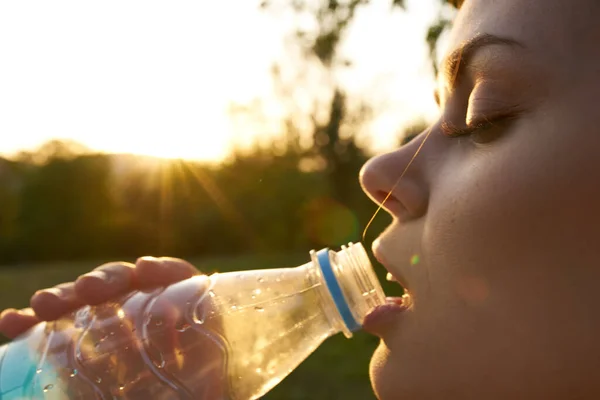 Kvinna dricker vatten från en plastflaska utomhus på sommaren — Stockfoto