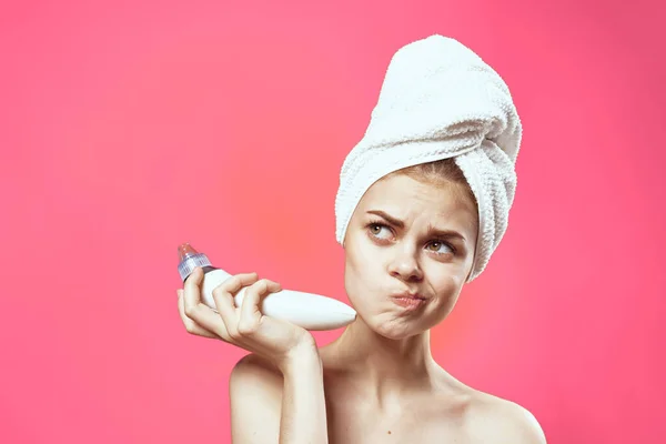 Mooie vrouw met een handdoek op haar hoofd massager in handen cosmetologie schone huid roze achtergrond — Stockfoto