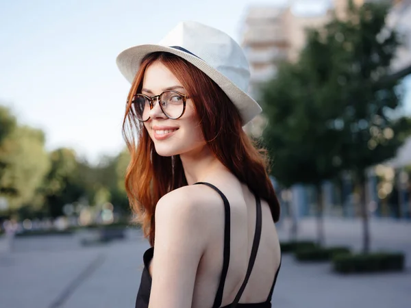 Mulher feliz em um chapéu branco e óculos caminha na natureza na rua — Fotografia de Stock