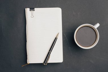 Koyu arka planda kalem ve bir fincan kahve ofisi manzaralı defter.