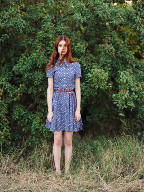 Çalılıkların yanındaki parkta kırmızı böğürtlenli ve mavi elbiseli bir kadın.