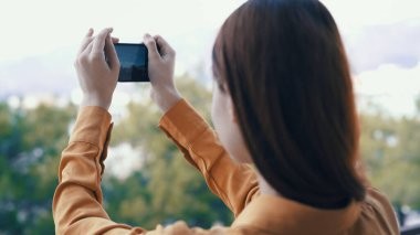 Dışarıda elinde telefon olan bir kadın kamerayla fotoğraf çekiyor.