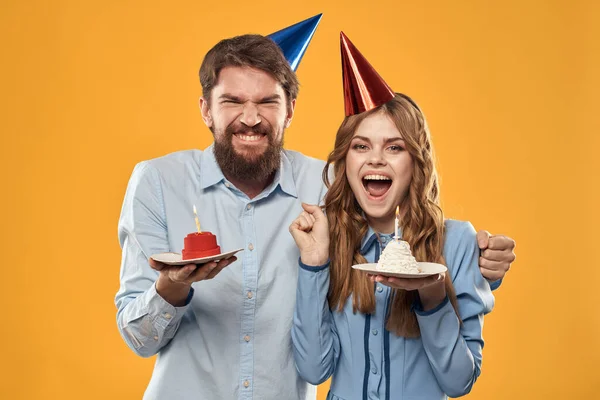 Homem e mulher em uma festa em bonés e com bolo de ouropel divertido fundo amarelo — Fotografia de Stock