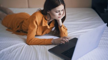 Kadın yatak odasında yatar dizüstü bilgisayarın önünde çalışır.