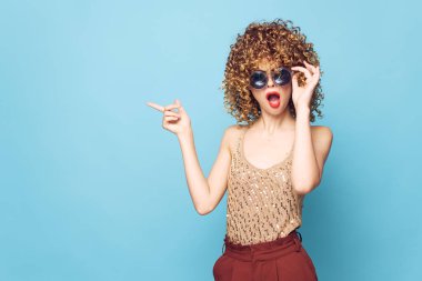 Model kıvırcık saçlar koyu gözlükler, elleri mavi arkaplan cazibesi 