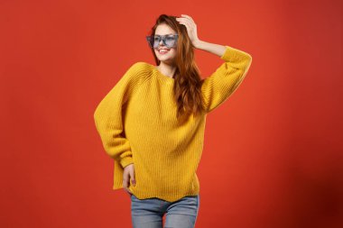 Neşeli kadın sarı süveter gözlüklü moda stüdyosu kırmızı arka plan