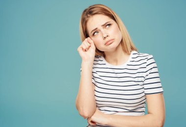 Mavi arka planda ağlayan ve elleriyle yüzüne dokunan sevimli sarışın kadın.