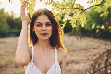 Doğadaki yeşil ağaçların yanında beyaz elbiseli romantik bir kadın.