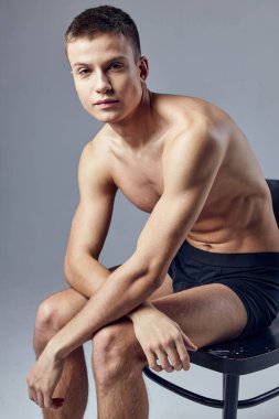 Şişirilmiş, siyah külotlu çıplak bir vücudu olan hoş bir adam bir sandalyede oturuyor.