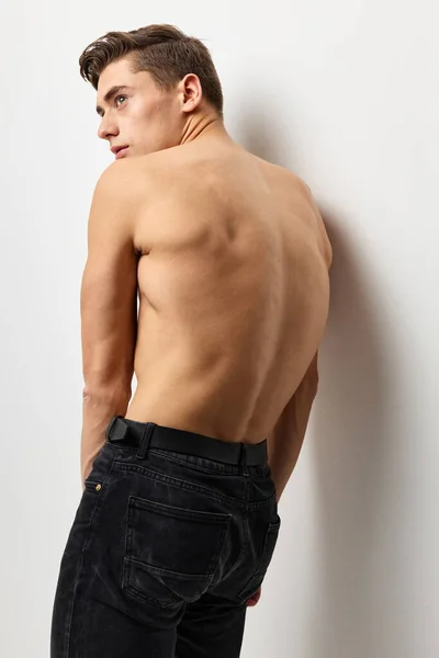 Handsome man stands with his back naked torso black pants posing — Stock Photo, Image