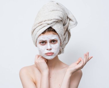 Kafasına havlu takmış, maske takmış omuzları çıplak cilt bakımı yapan bir kadın.