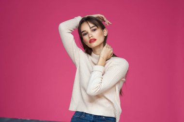 Uzun saçlı, kırmızı dudaklı beyaz bluzlu, pembe arka planlı çekici bir kadın.