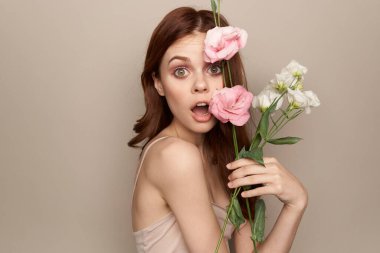 Bej arka planda bir buket hafif çiçekle mutlu bir kadın. Çıplak omuzlar, güzel kızıl saçlar.