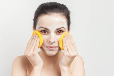 Çıplak omuzlu bir kadın maskesini yüzüne süngerle siler.