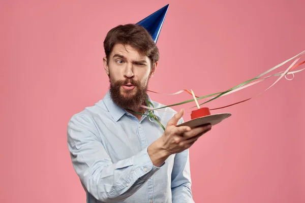 Homme barbu avec langue de gâteau sur un fond rose vue recadrée et une casquette bleue sur sa tête — Photo