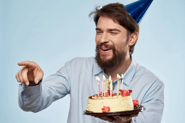 Un hombre con una camisa con un pastel en las manos y una gorra festiva en la cabeza — Foto de Stock