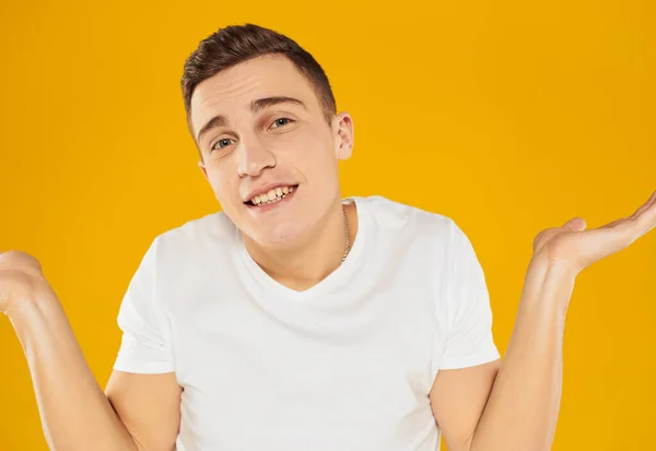 A guy in a white T-shirt spreads his arms to the sides on a yellow background emotions model — Stock Photo, Image
