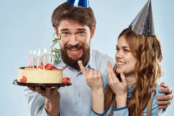 Birthday man woman in party hats on a blue background and cake with candles