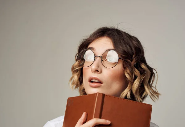 Romantische Frau mit Brille auf grauem Hintergrund und einem braunen Buch in der Hand — Stockfoto