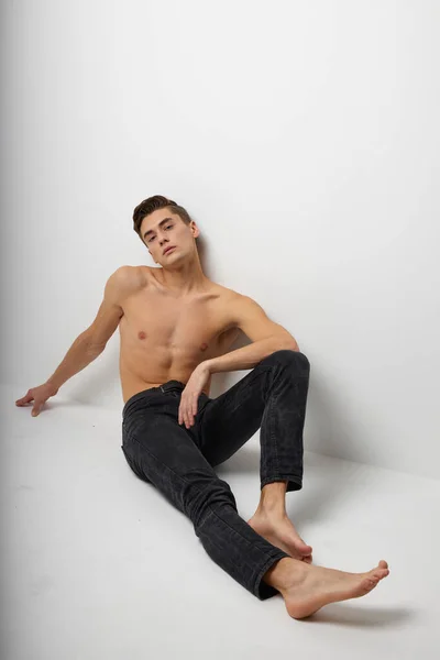 Bonito homem sentado no chão preto calças nu torso posando — Fotografia de Stock