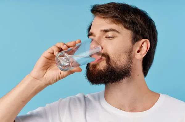 Homem bonito bebendo água de um copo em um fundo azul close-up retrato — Fotografia de Stock