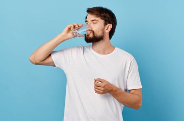 Mavi arka planda bir bardak suyu olan beyaz tişörtlü adam.