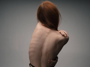 Çıplak kadın el kol hareketleri yapıyor. Kızıl saçlı, açık renk arka plan.