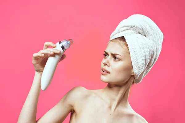 Pretty woman with a towel on her head massager in hands cosmetology clean skin pink background — Stock Photo, Image