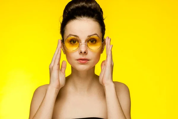 Atraktivní žena s holými rameny nosí brýle shromážděné vlasy úsměv žluté pozadí — Stock fotografie