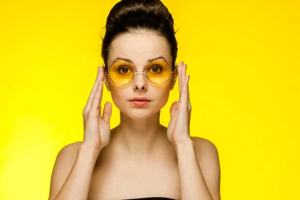 Attrayant femme avec les épaules nues portant des lunettes recueilli cheveux sourire fond jaune — Photo