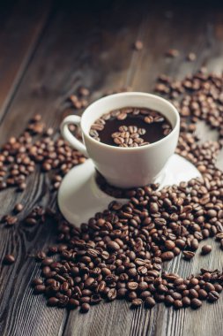 Tahta bir masada bir fincan sıcak kahve ve serpiştirilmiş fasulye.