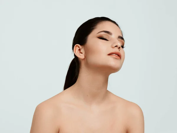 Mulher atraente com ombros nus em um fundo leve olha para o lado — Fotografia de Stock