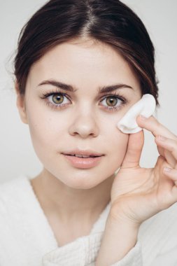 Bornozlu bir kadın yüzünü süngerle siliyor. Temiz bir cilt kozmetolojisi.