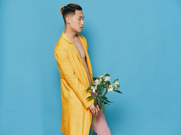 Vista lateral de um homem asiático atraente em um casaco amarelo e em calças rosa com um buquê de flores em sua mão — Fotografia de Stock