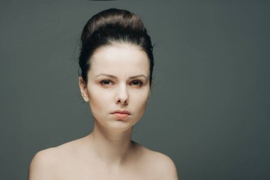 Çekici esmer, çıplak omuzlu, açık tenli, gri arka planlı.