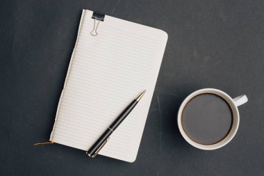 Koyu arka planda kalem ve bir fincan kahve ofisi manzaralı defter.
