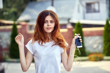 Beyaz tişörtlü bir kadın sokakta kulaklıkla yürüyor.