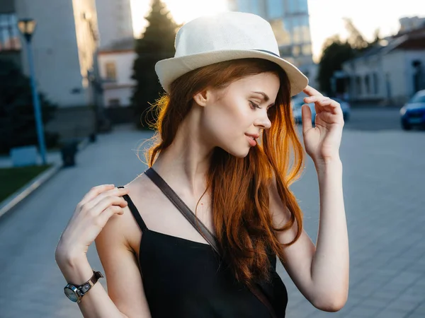Eine schöne Frau mit roten Haaren, weißem Hut und schwarzem Kleid auf der Straße in der Stadt — Stockfoto