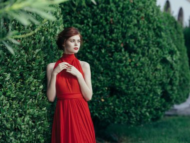 Güzel bayan kırmızı elbise yeşil çalı dışarıda lüks prenses yürüyor.